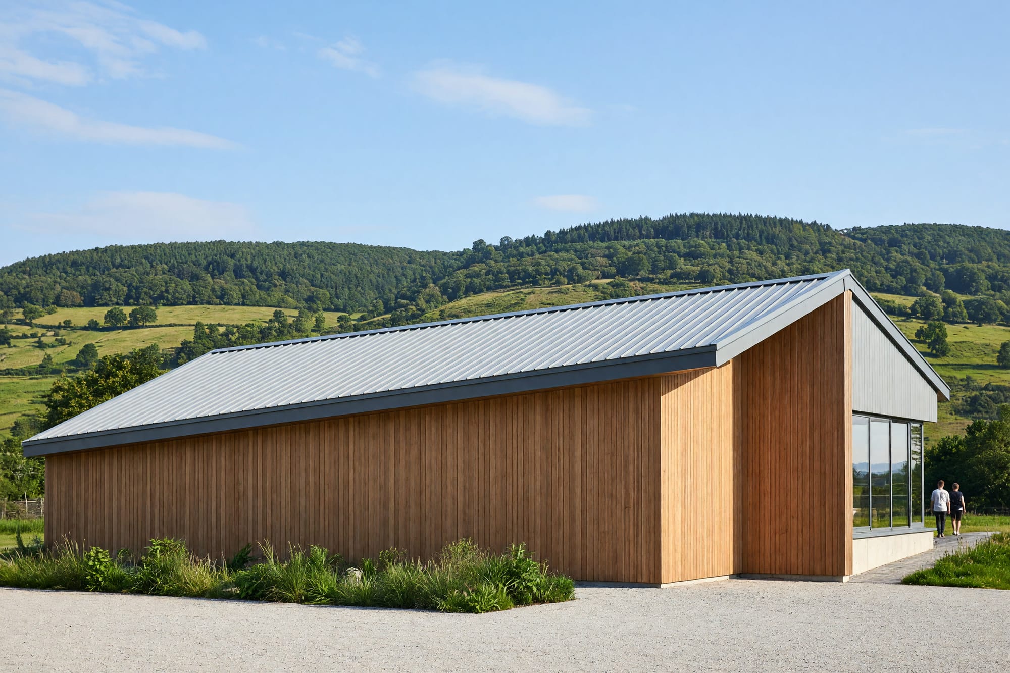 A long low industrial building in vertical timber cladding and profiled metal with hills behind