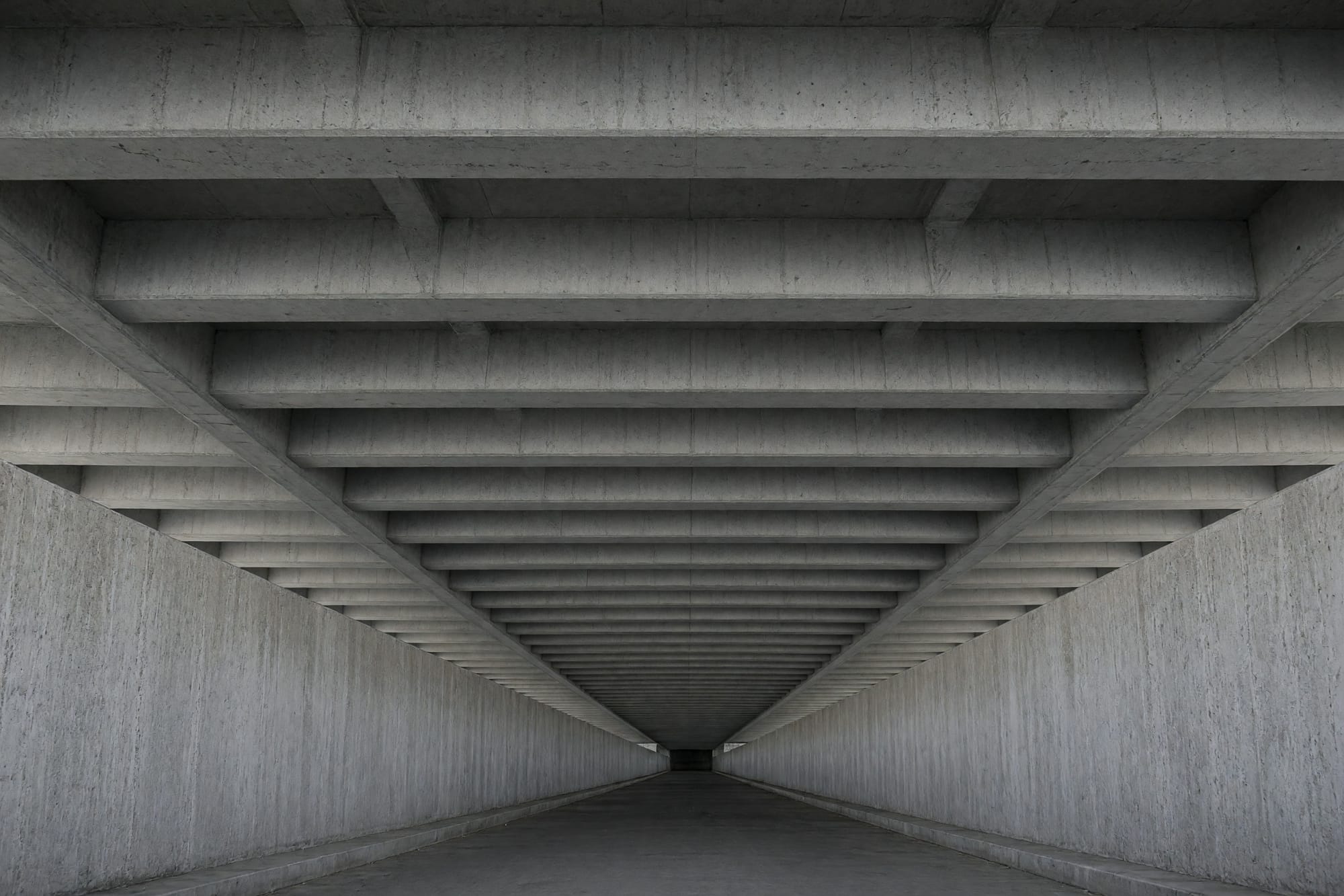 The underside of a concrete walkway bridge with the beams converging