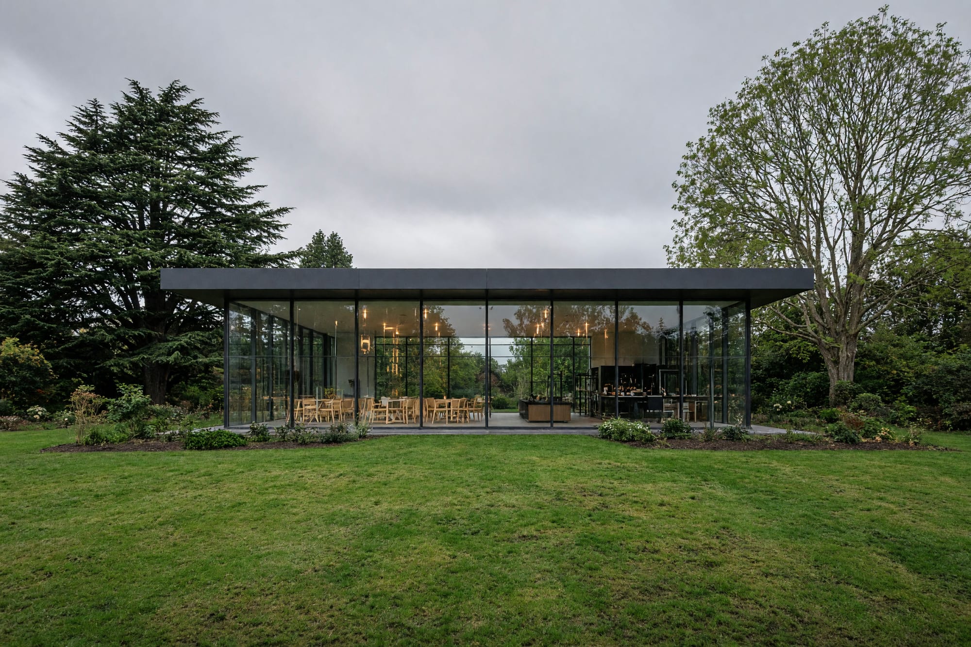 A modern glazed pavilion in a botanic garden seen across a lawn