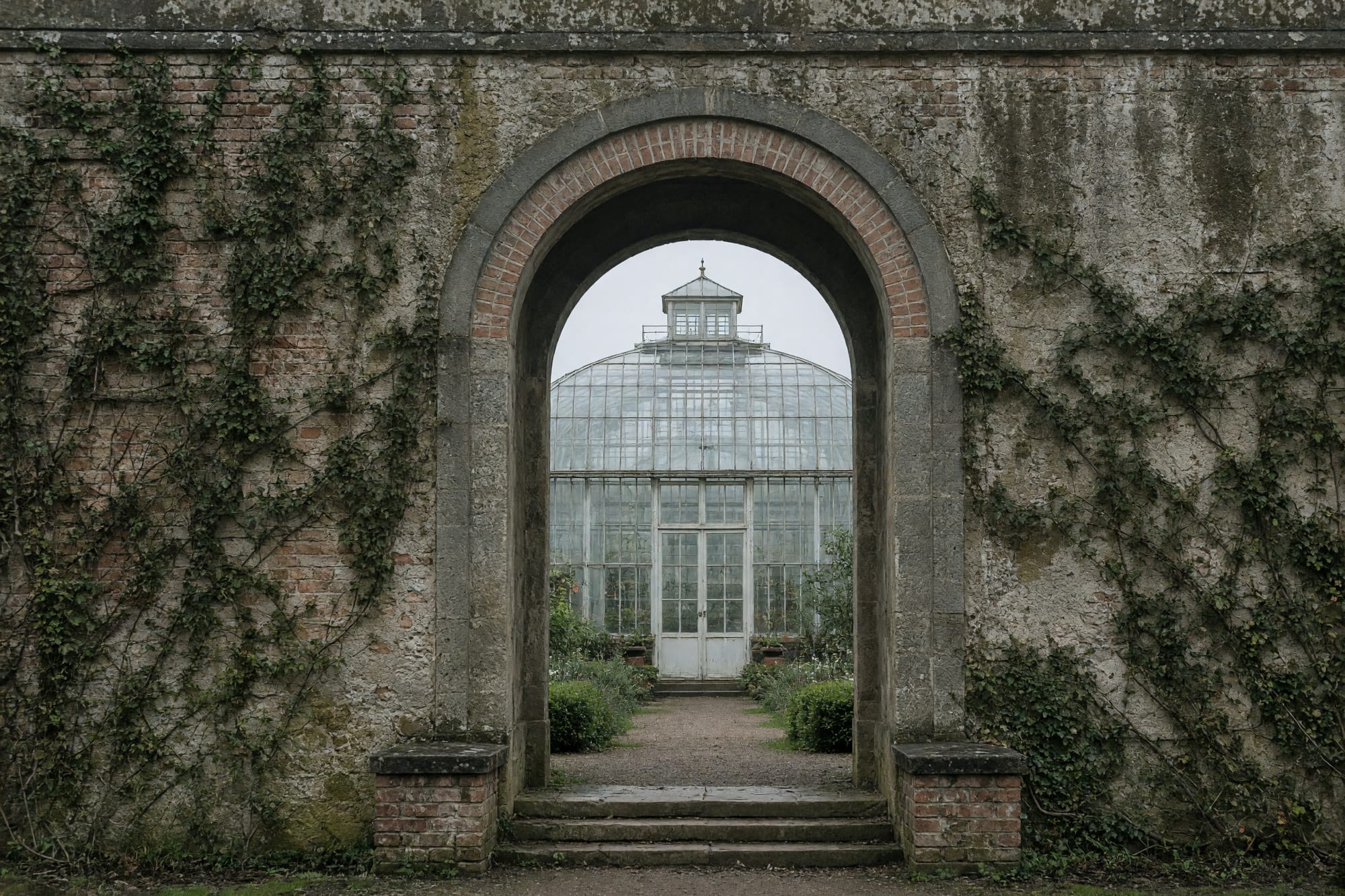 A walled garden doorway framing a glasshouse beyond it