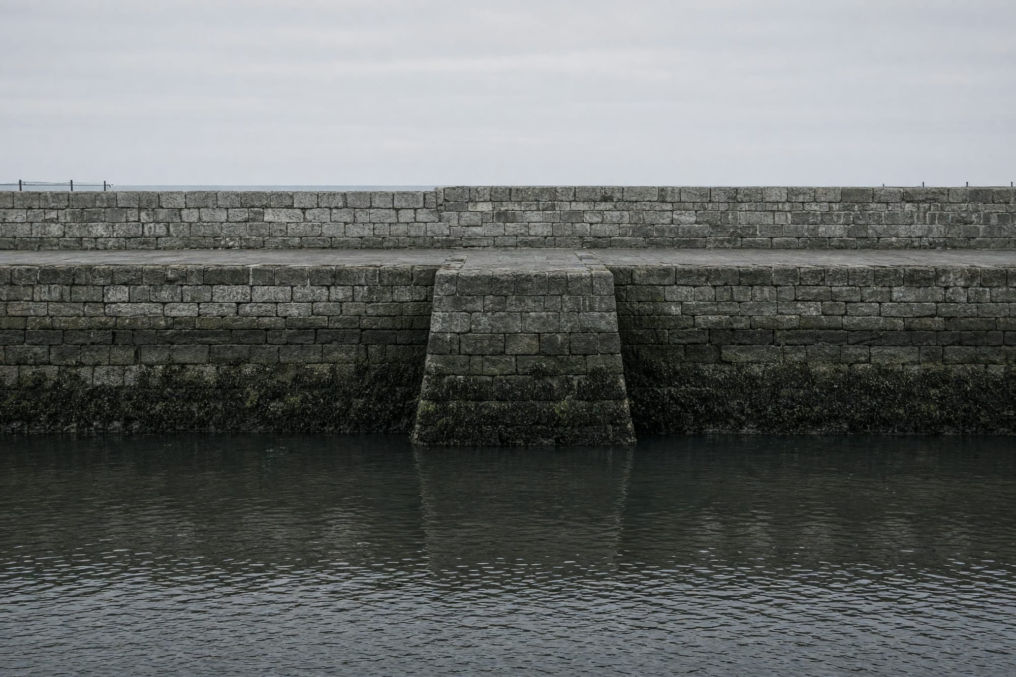 A harbour wall stepping into the water with the tide line legible on the stone