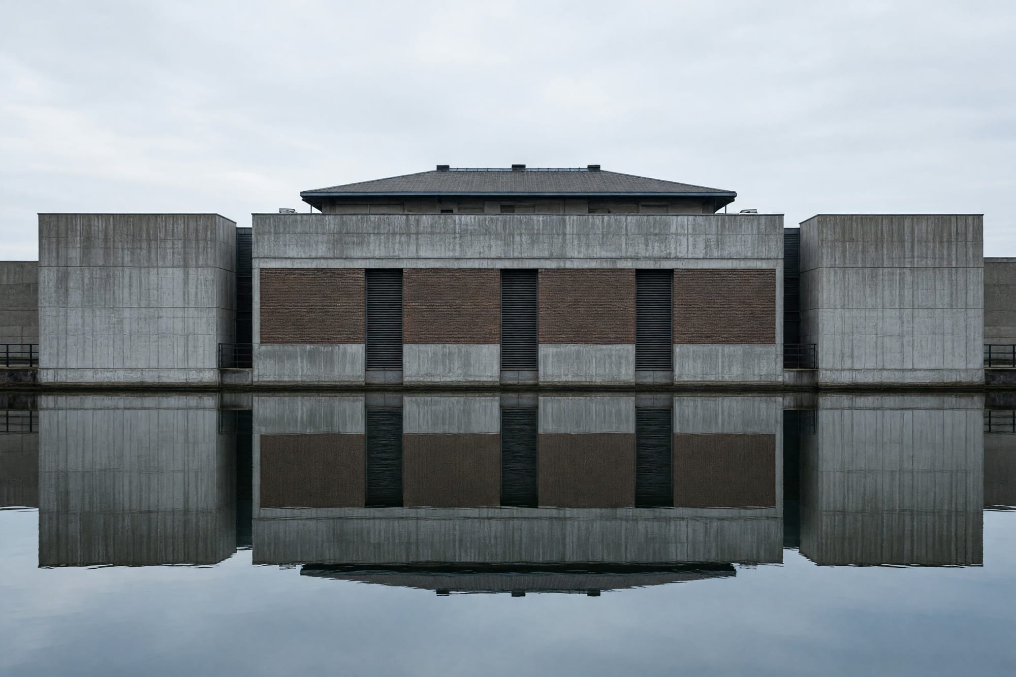 A pumping station elevation seen across a still channel, doubled in the reflection