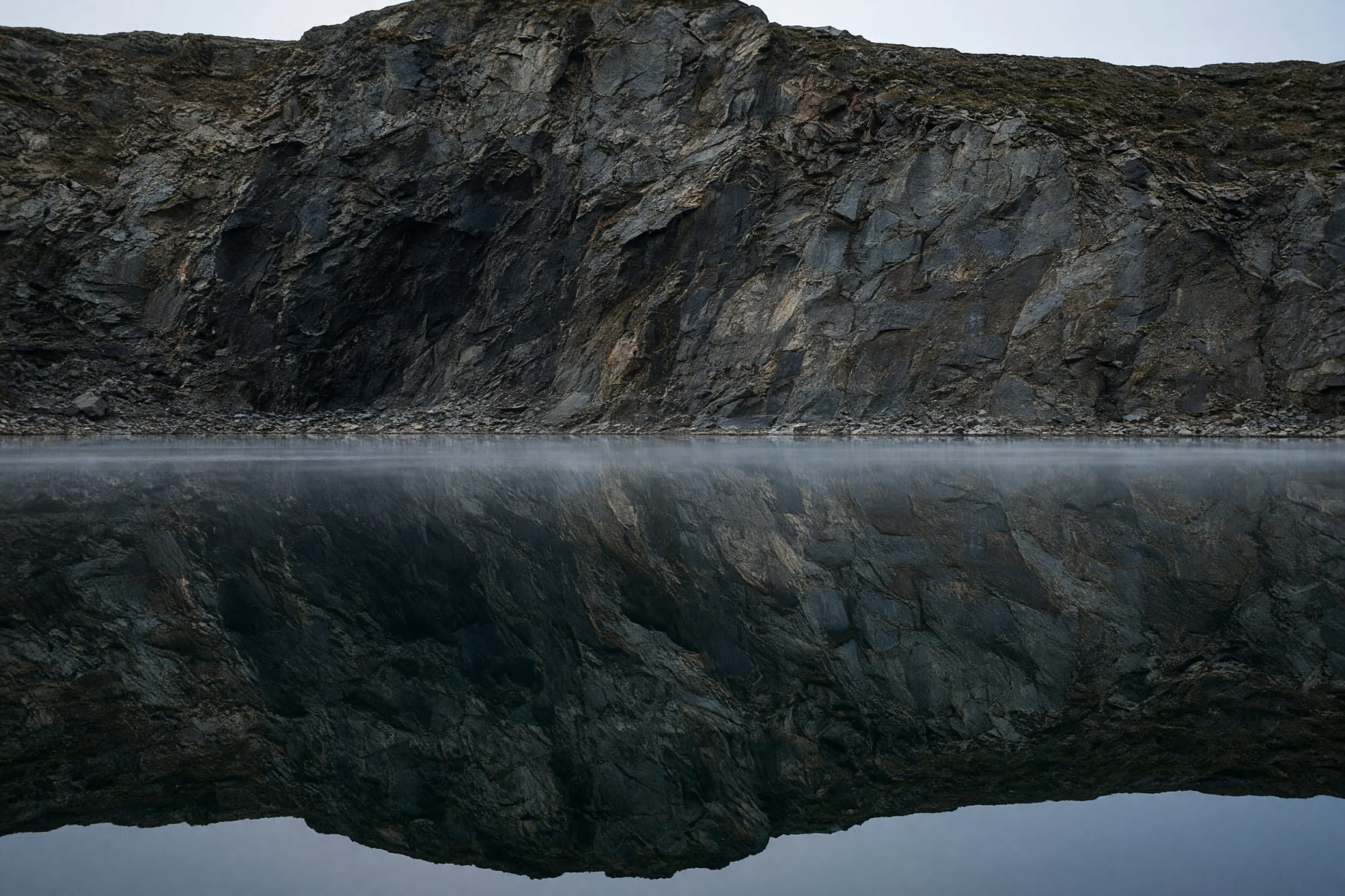 A flooded quarry with a sheer rock face doubled in glassy water